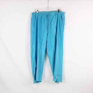 Könnte beinhalten: Türkisblaue Hose mit Kordelzug in der Taille und Knopfdetails an den Knöcheln. Die Hose aus leichtem Stoff hängt an einem Kleiderbügel vor weißem Hintergrund.