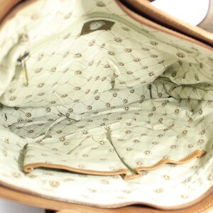 May include: An open tan leather tote bag. The interior is lined with light green fabric patterned with a repeating emblem. A zipped pocket and other pockets are visible. The bag has a rectangular shape.