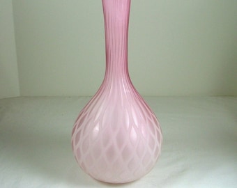 May include: A pink glass vase with a textured, diamond-shaped pattern. The vase has a long, slender neck and a rounded base.