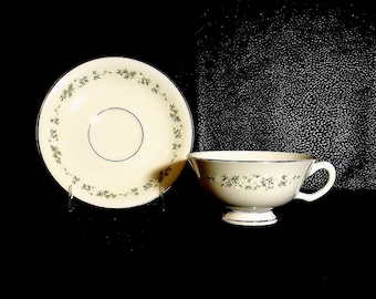 Puede incluir: Una taza de té y un platillo blancos con un delicado patrón floral en tonos verdes y blancos. El platillo tiene un fino borde dorado.