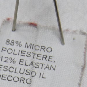 May include: White fabric label with black text that reads "88% Micro Poliestere, 12% Elastan Escluso il Decoro".