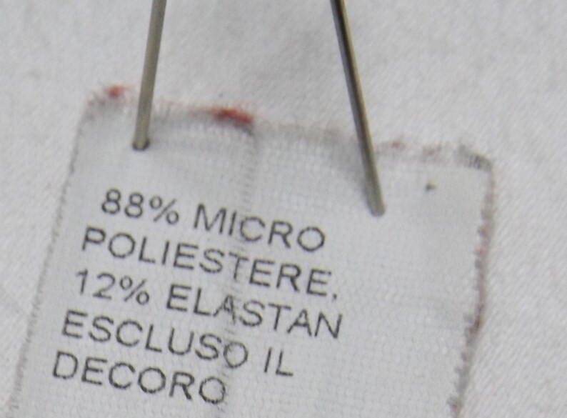 May include: White fabric label with black text that reads "88% Micro Poliestere, 12% Elastan Escluso il Decoro".