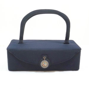 May include: A navy blue rectangular handbag with a single top handle and a decorative metal clasp with a floral design.