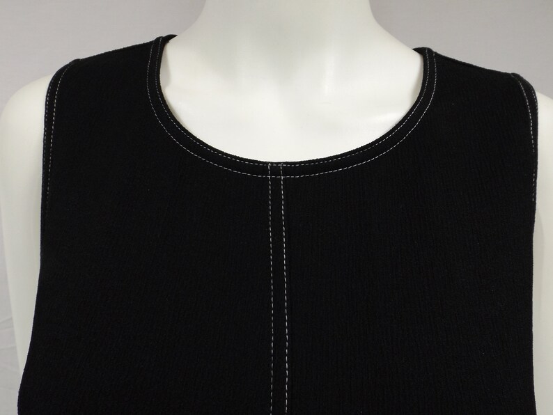 May include: Black sleeveless top with white stitching around the neckline and down the center front.