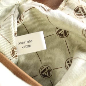 May include: Close-up of the interior of a brown leather bag. The lining is a light beige fabric with a repeating brown logo pattern. A white tag reads "Genuine Leather" and "ASI 93990".
