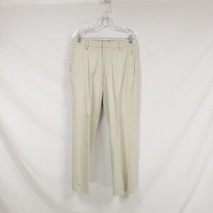 May include: A pair of beige casual trousers hanging on a white hanger. The trousers have a straight leg and a flat front.