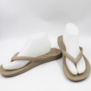 May include: A pair of tan flip-flops with a simple design. The flip-flops are made of a soft, flexible material and have a comfortable footbed.