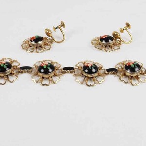May include: A gold bracelet with black and red enamel floral accents and matching clip-on earrings. The bracelet has a chain extension.