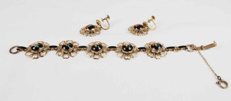 May include: A gold bracelet with black and red enamel floral accents and matching clip-on earrings. The bracelet has a chain extension.