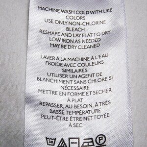 May include: White care label with instructions for washing, drying, and ironing a garment. The label includes both English and French instructions. The text reads "Machine wash cold with like colors. Use only non-chlorine bleach. Reshape and lay flat to dry. Low iron as needed. May be dry cleaned. Laver &agrave; la machine &agrave; l'eau froide avec couleurs similaires. Utiliser un agent de blanchiment sans chlore si n&eacute;cessaire. Mettre en forme et s&eacute;cher &agrave; plat. Repasser, au besoin, &agrave; tr&egrave;s basse temp&eacute;rature. Peut-&ecirc;tre &ecirc;tre nettoy&eacute;e &agrave; sec."