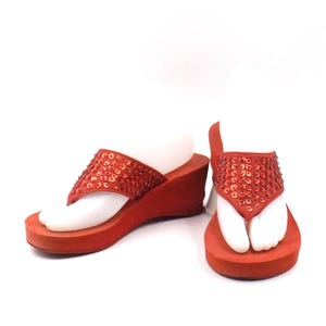 May include: Red wedge sandals with a thong strap adorned with sequins. The sandals have a platform sole and a heel. The shoes are displayed on a white background.