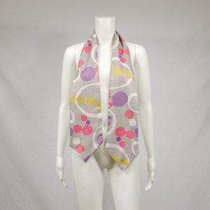 May include: A white scarf with a geometric pattern of pink, purple, and yellow circles on a gray background.