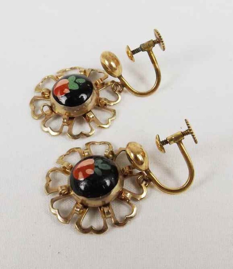 May include: A pair of gold tone clip-on earrings with black and red enamel flower designs.