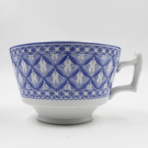 May include: A white teacup with a blue and white geometric pattern. The cup has a handle and a rounded shape.