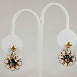 May include: A pair of gold tone earrings with a black and red floral design. The earrings are on a white display stand.