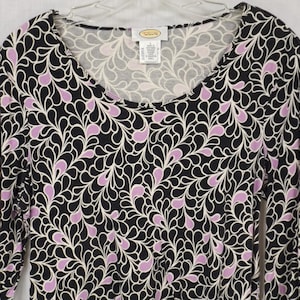 May include: Black long-sleeve shirt with a white and purple paisley pattern. The shirt has a scoop neck and is made of a soft, stretchy fabric.