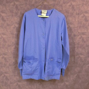 May include: A light blue medical scrub top with long sleeves, a button-up front, and two pockets. The top has the brand name "Landau" on the left side of the collar and on the right pocket.