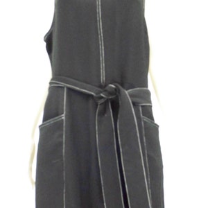 May include: A black sleeveless jumpsuit with a white top stitch detail. The jumpsuit has a self-tie belt and two large pockets on the front.