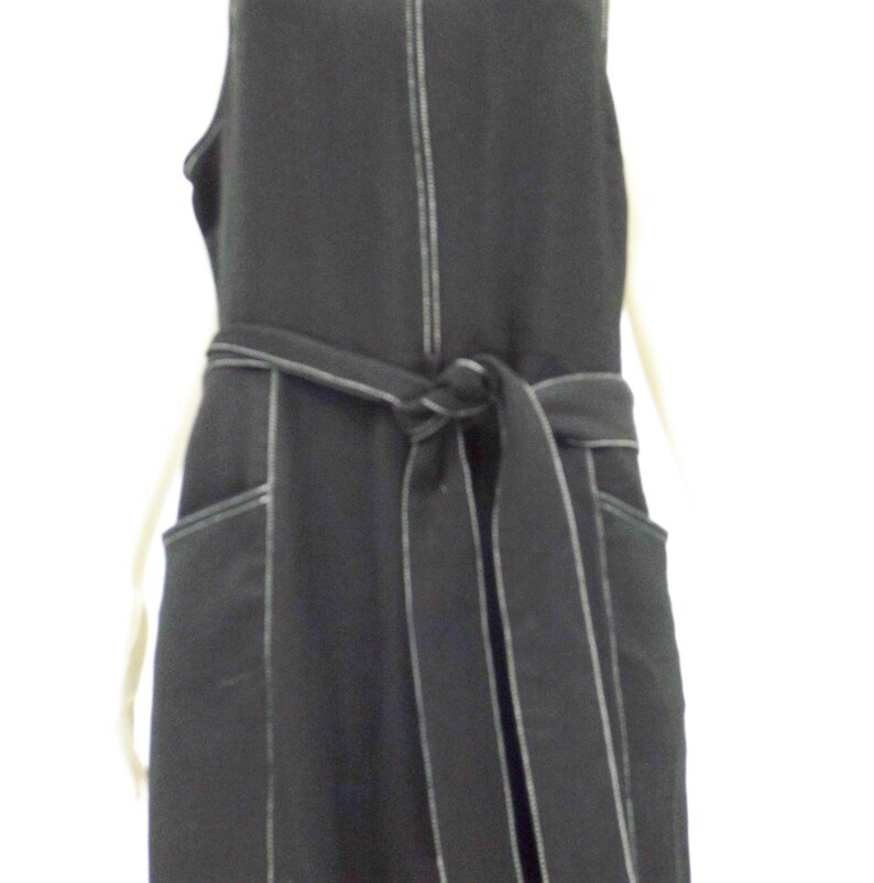 May include: A black sleeveless jumpsuit with a white top stitch detail. The jumpsuit has a self-tie belt and two large pockets on the front.