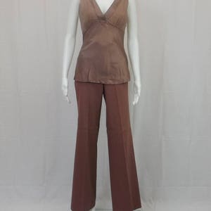 Puede incluir: Una blusa sin mangas con cuello en V y pantalones de pierna ancha de color marrón. La blusa tiene un brillo satinado.