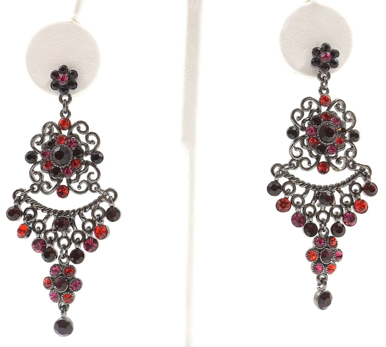 May include: A pair of dangle earrings with a black metal filigree design and red and pink crystals.
