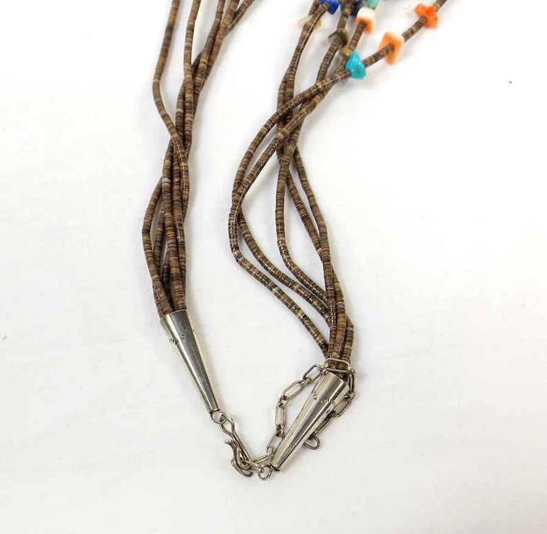 May include: A multi-strand necklace made of brown seed beads with a silver clasp. The necklace is adorned with colorful stones, including turquoise, coral, and lapis lazuli.