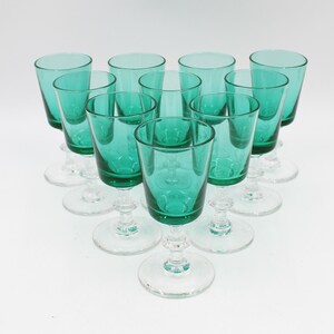 May include: A collection of ten emerald green stemmed glasses. Each glass has a clear, round base and a decorative stem. The glasses are arranged in a circular pattern, showcasing their vibrant color and elegant design. Ideal for serving beverages.