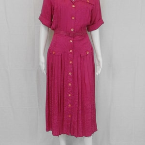 May include: A pink button-down dress with a belt and a pleated skirt. The dress has a floral pattern and short sleeves.