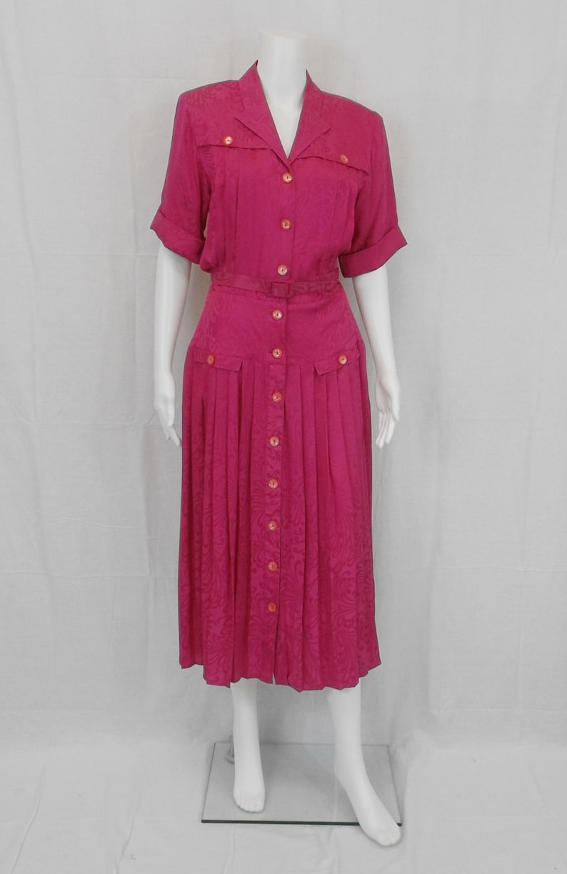 May include: A pink button-down dress with a belt and a pleated skirt. The dress has a floral pattern and short sleeves.