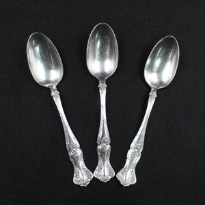 May include: Three silver spoons with ornate handles. The spoons have a polished finish and are decorated with a floral design.
