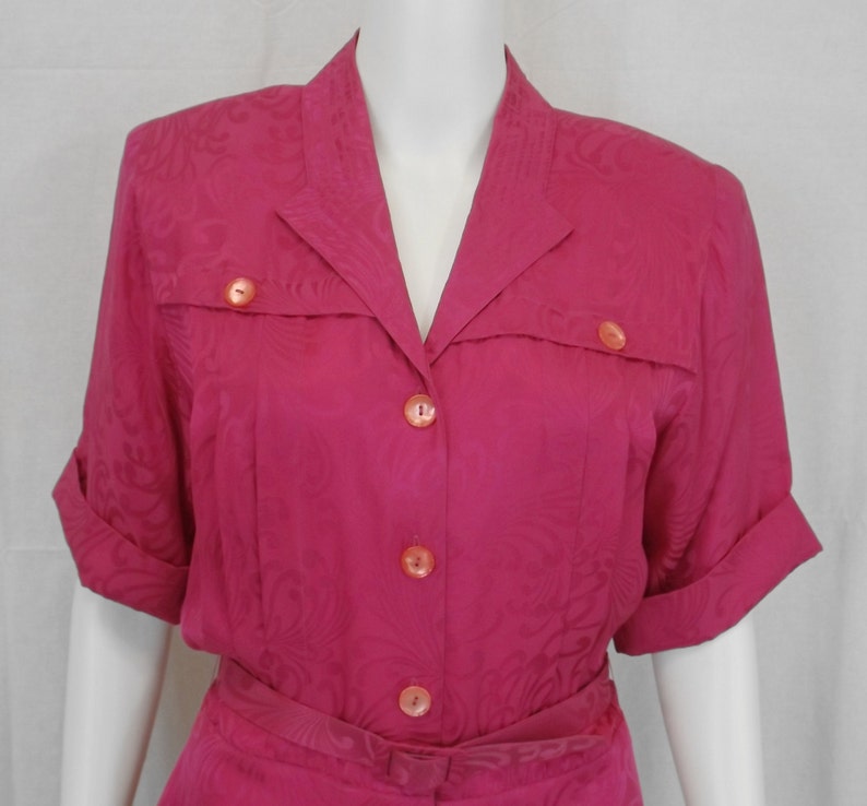 May include: A pink short-sleeved dress with a collared neckline and a button-up front. The dress has a floral pattern and a belt.