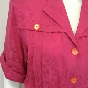 May include: A pink button-up shirt with a floral pattern and orange buttons. The shirt has a collar and short sleeves.