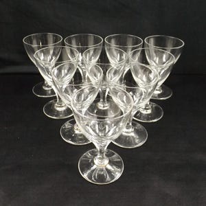 Może przedstawiać: Zestaw dziesięciu przezroczystych szklanek do wina z delikatną nóżką i szeroką czaszą.