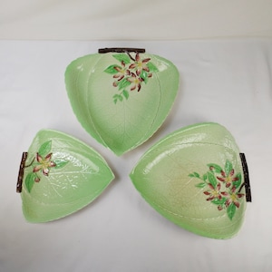 Puede incluir: Tres platos de servir de hoja verde con asas marrones y diseños florales. Los platos son de cerámica y tienen una superficie texturizada.