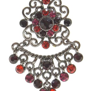 May include: A pair of dangle earrings with a black metal filigree design. The earrings feature red, pink, and black crystals.