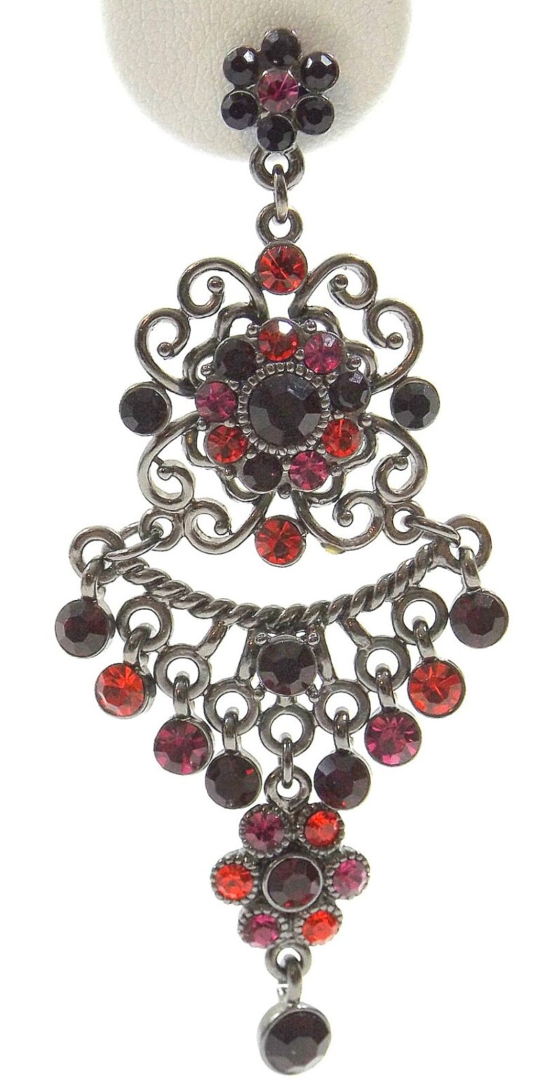 May include: A pair of dangle earrings with a black metal filigree design. The earrings feature red, pink, and black crystals.