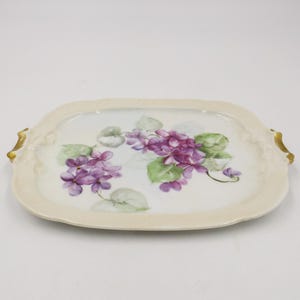 May include: A white porcelain serving tray with gold accents and a hand-painted design of purple violets and green leaves.
