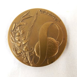 Puede incluir: Una medalla de bronce con un dise&ntilde;o de una rama de olivo y una cinta con el texto hebreo "לשחרור" (para la liberaci&oacute;n) en el borde.