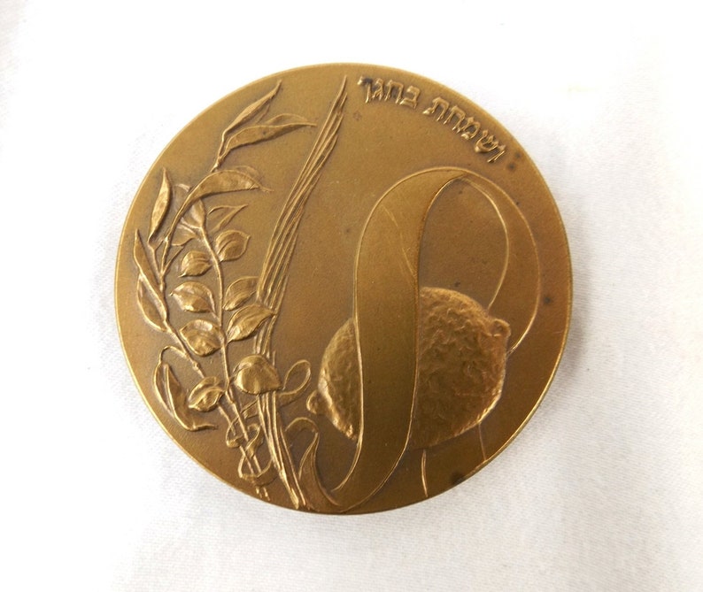 Puede incluir: Una medalla de bronce con un dise&ntilde;o de una rama de olivo y una cinta con el texto hebreo "לשחרור" (para la liberaci&oacute;n) en el borde.