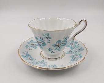 May include: A white teacup and saucer set with a blue and gold floral pattern. The cup has a fluted rim and a delicate handle. The saucer has a scalloped edge.