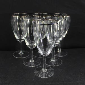 Può includere: Set di otto bicchieri da vino in vetro trasparente con bordo argentato.