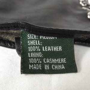 以下が含まれることがあります： 「SIZE: MEDIUM」、「SHELL: 100% LEATHER」、「LINING: 100% CASHMERE」、「MADE IN CHINA」と白文字で書かれた緑色のラベルです。