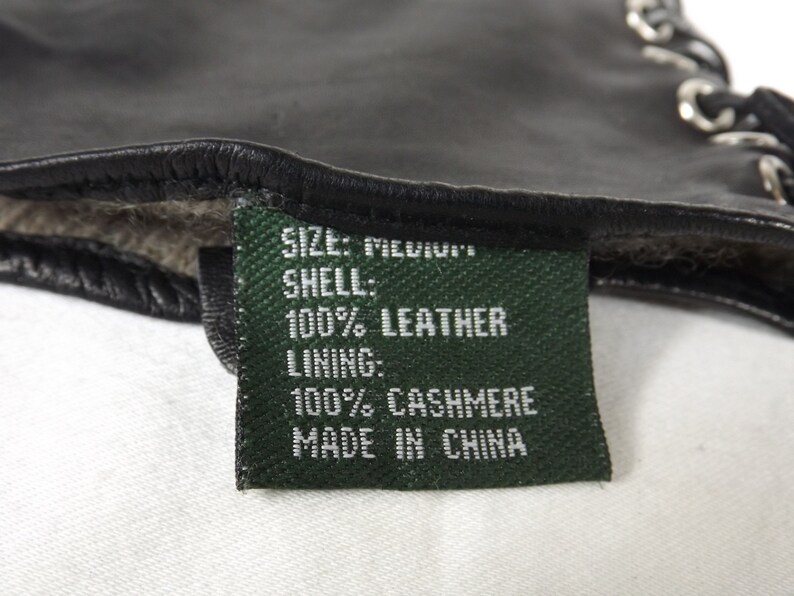 以下が含まれることがあります： 「SIZE: MEDIUM」、「SHELL: 100% LEATHER」、「LINING: 100% CASHMERE」、「MADE IN CHINA」と白文字で書かれた緑色のラベルです。