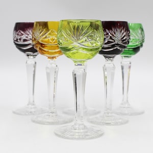 May include: Set of six stemmed shot glasses with cut glass designs. The glasses are in various colors, including purple, orange, green, and clear.