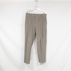 May include: A pair of light brown corduroy trousers hanging on a white hanger against a white background.