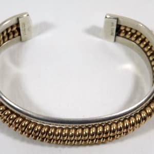May include: A silver and gold bangle bracelet with a twisted design. The bracelet is open and has a hinge.