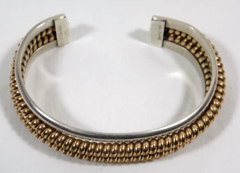 May include: A silver and gold bangle bracelet with a twisted design. The bracelet is open and has a hinge.