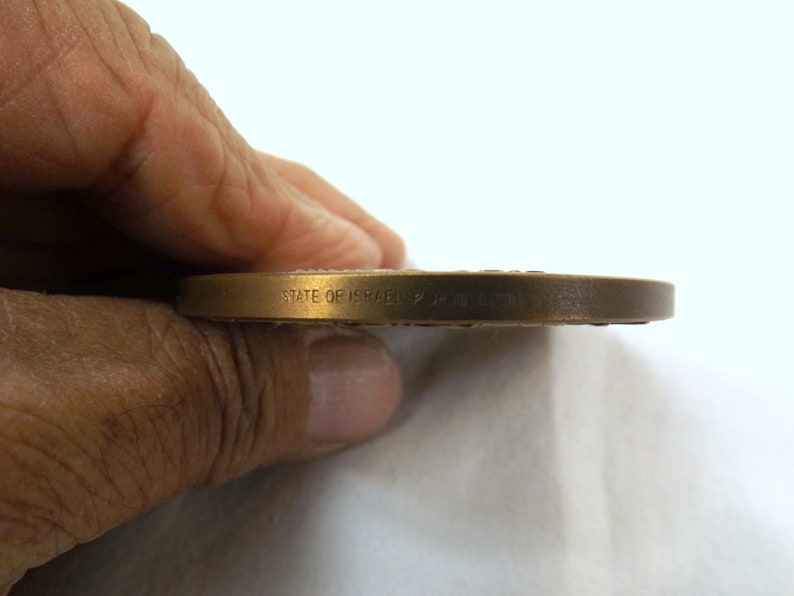 Puede incluir: Primer plano del borde de una moneda de bronce con la inscripci&oacute;n "STATE OF ISRAEL" en el lateral.