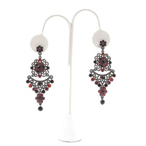 May include: A pair of dangle earrings with a black metal filigree design and red and burgundy crystals.