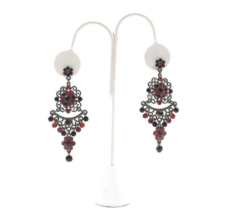 May include: A pair of dangle earrings with a black metal filigree design and red and burgundy crystals.